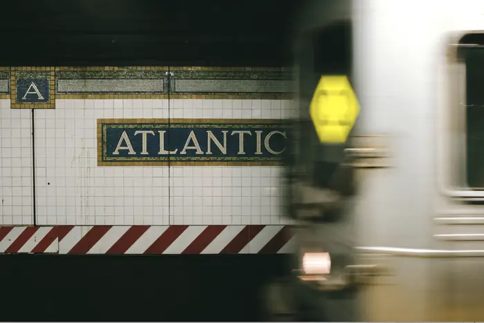 A blurry shot of the Q train pulling into Atlantic Avenue station with the name of the station in tilework behind the train.